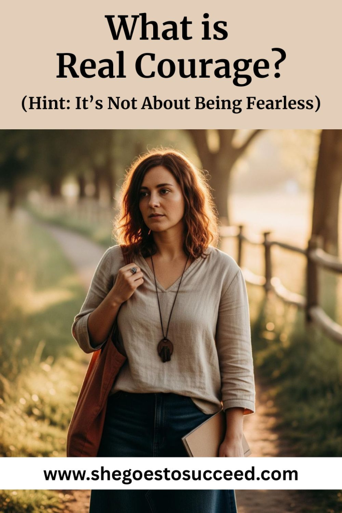 A woman is walking along a tree-lined path, holding a notebook. She has shoulder-length hair and is wearing a light, long-sleeved top with a necklace. The setting sun creates a warm, soft light.